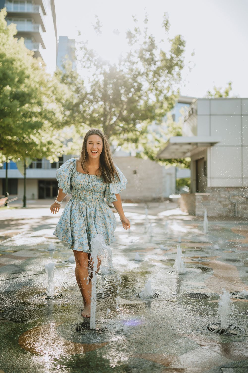 Someone enjoying a summer day playing in water fountains by a modern city building.