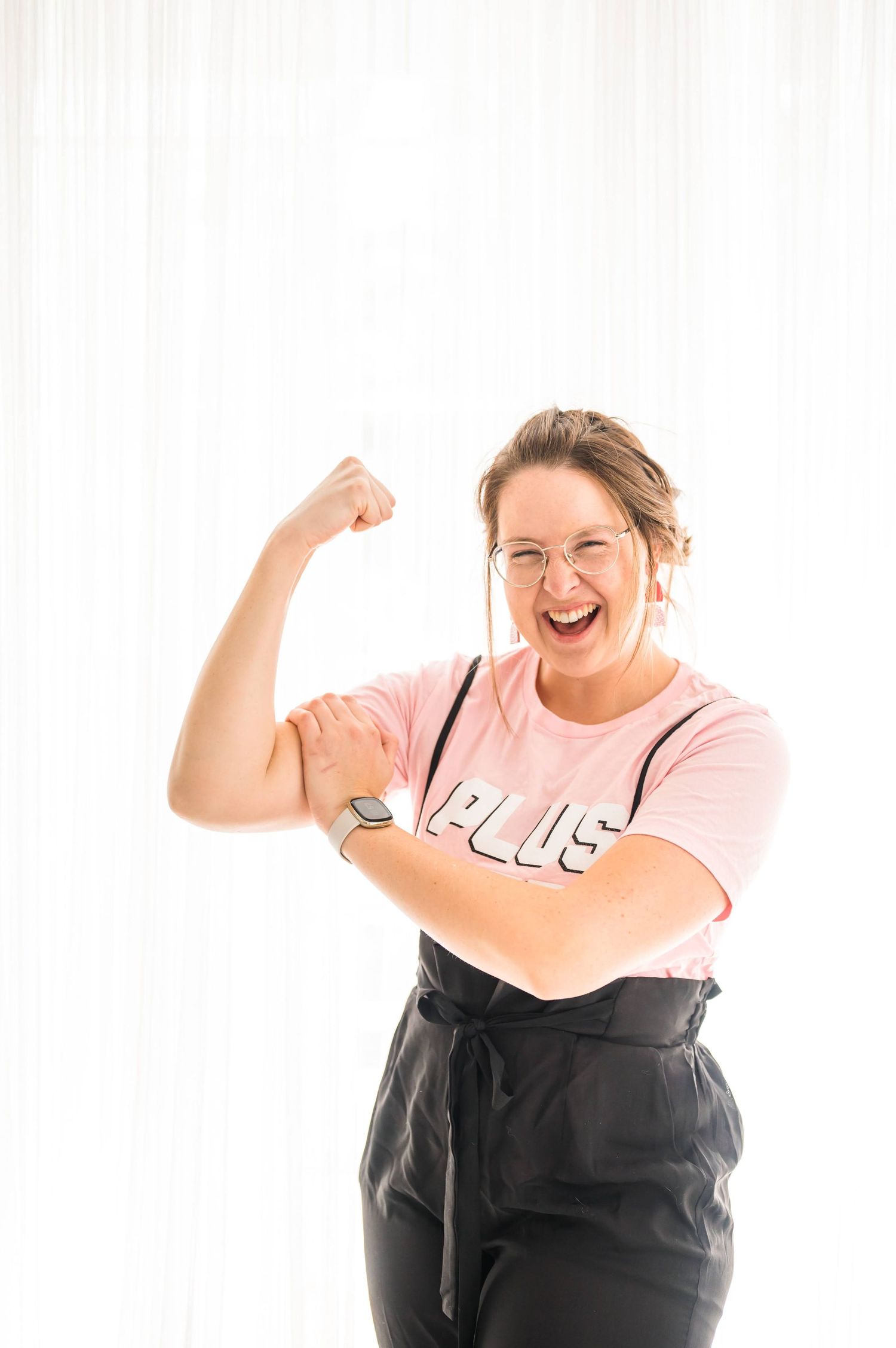 woman in pink shirt and overalls flexing her bicep and smiling at the camera