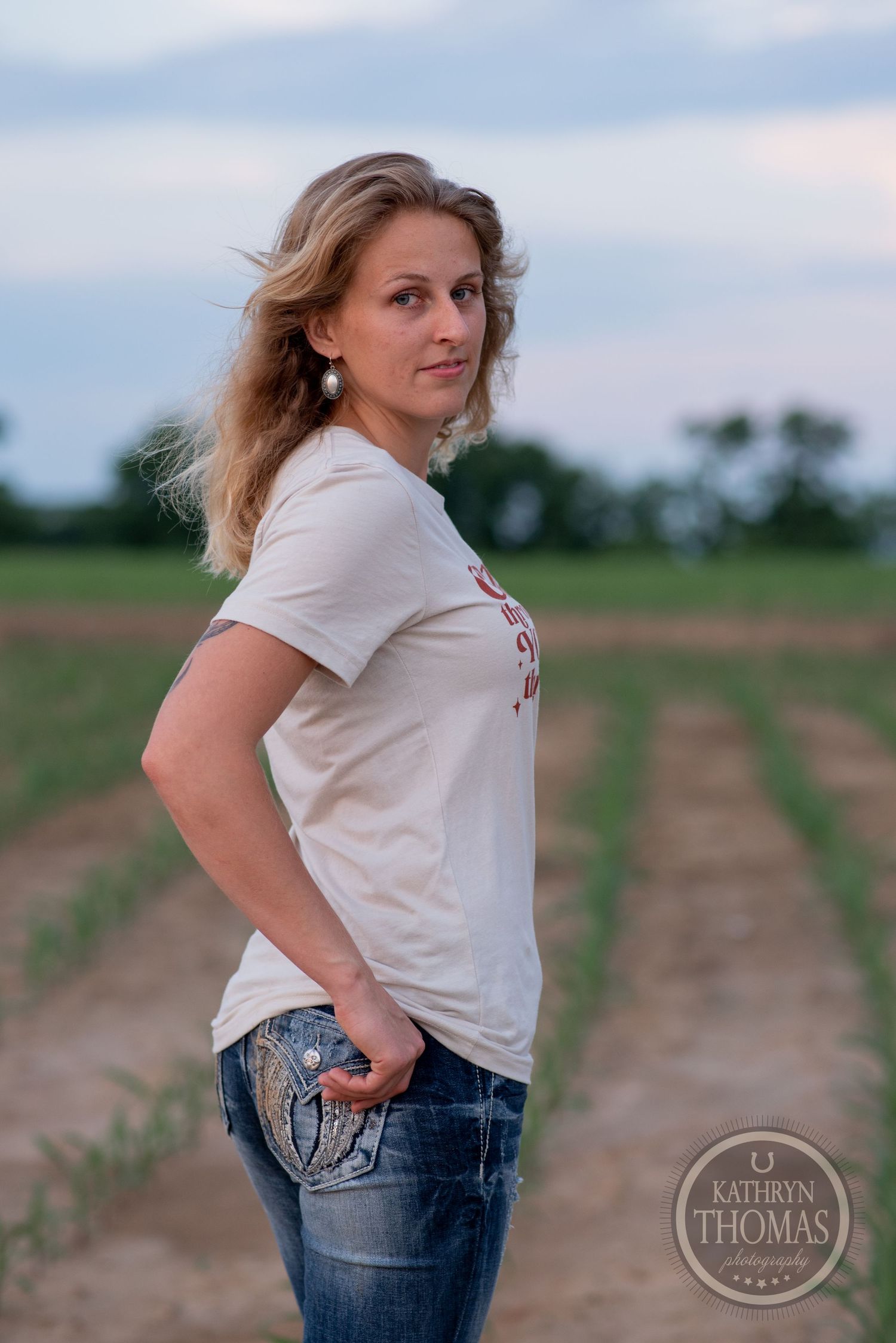 Casual portrait in farm field with rows of young crops visible in background.