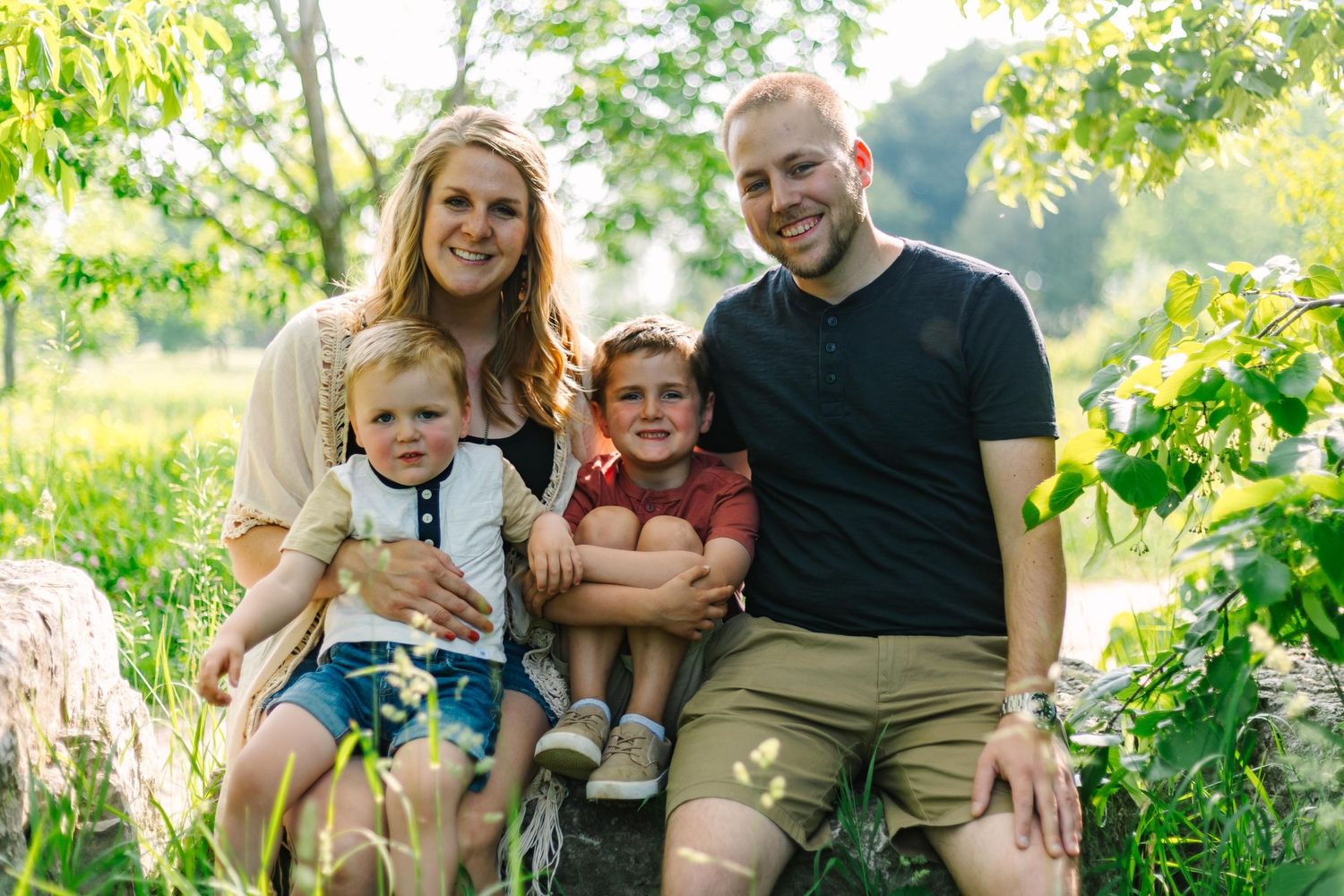 A family enjoys a sunny outdoor portrait session in a lush garden setting.