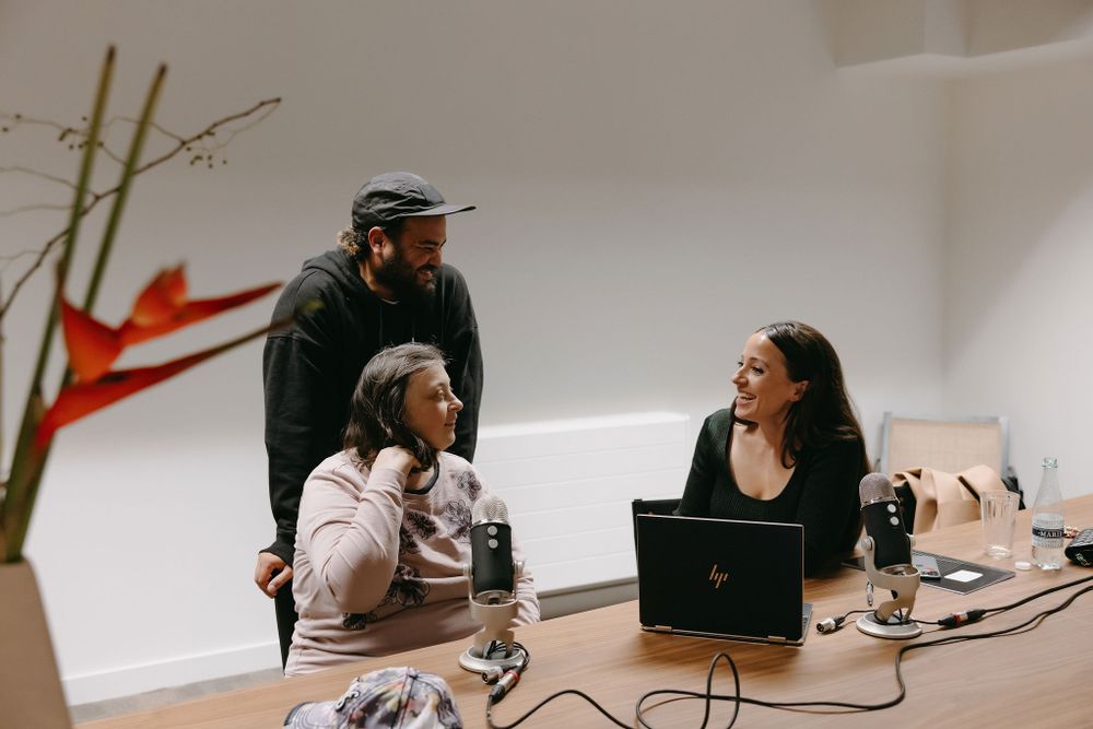 Casual office meeting with three people around laptop and microphones.