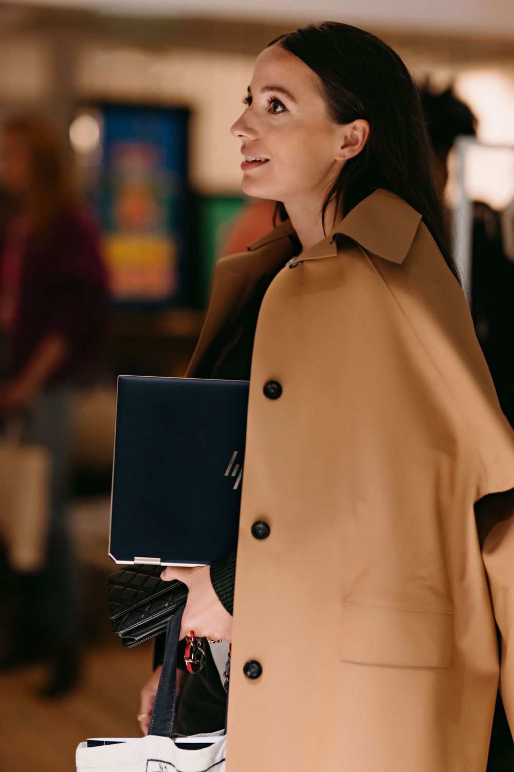 Side view of person in tan coat carrying laptop through office space.