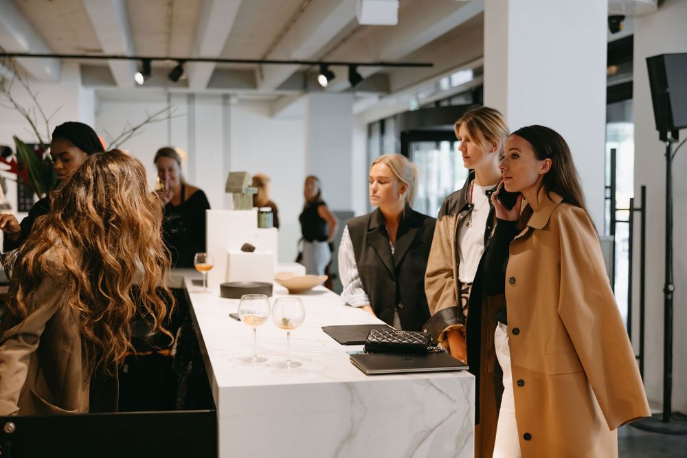 Fashion event attendees gather around a white table display in a modern industrial space.