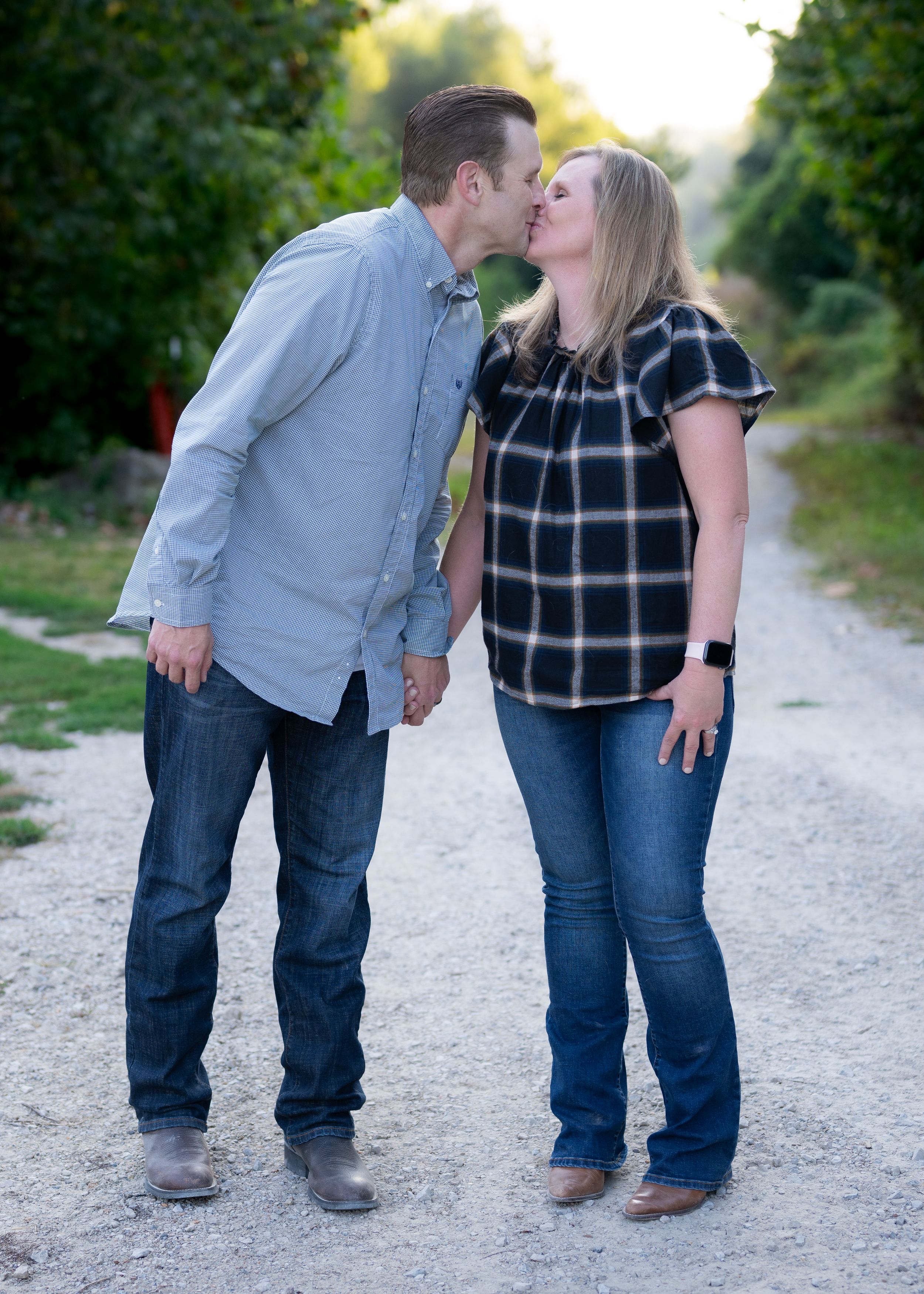 A couple shares a tender moment on a sunlit dirt path surrounded by greenery.