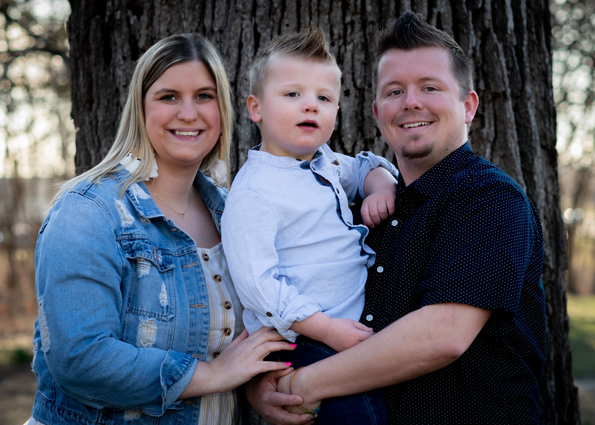 A family poses together in front of a large tree trunk.