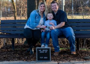 A family sits together on a wooden bench with a small chalkboard sign.