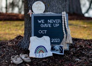 A pregnancy announcement display with rainbow onesie, sonogram and 'We Never Gave Up' sign.