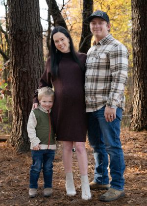 Family of three poses together in autumn forest wearing casual attire.