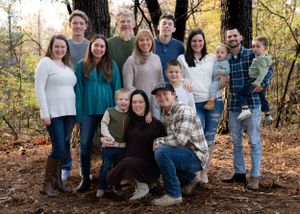 Large group poses together for family photo in wooded autumn setting.