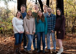 Family group stands together among fall trees wearing coordinated casual outfits.