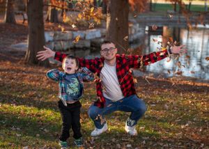 Two people strike playful poses while jumping on an autumn day near a pond.