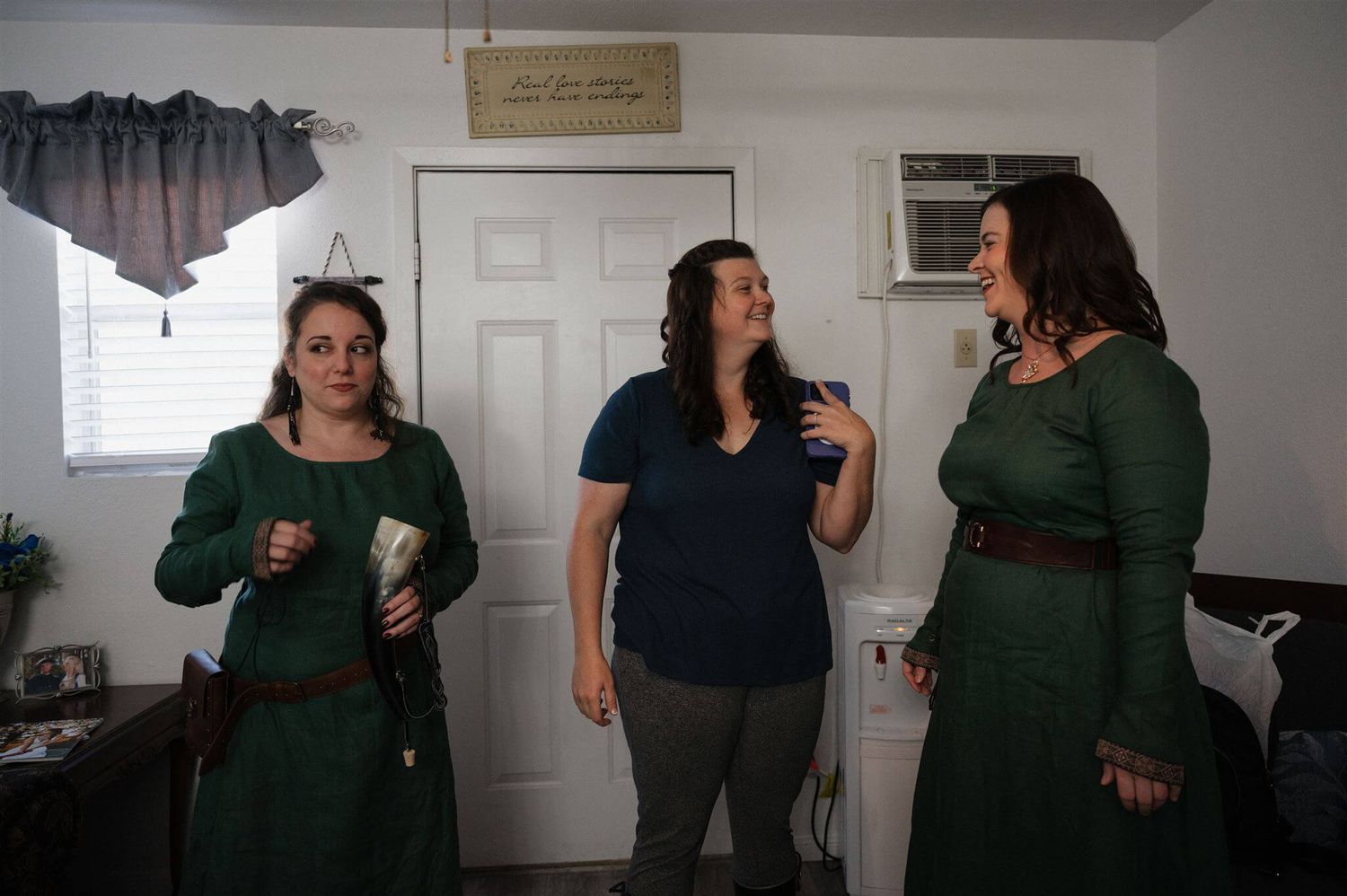 Three women in casual attire chat and laugh together in a home setting.