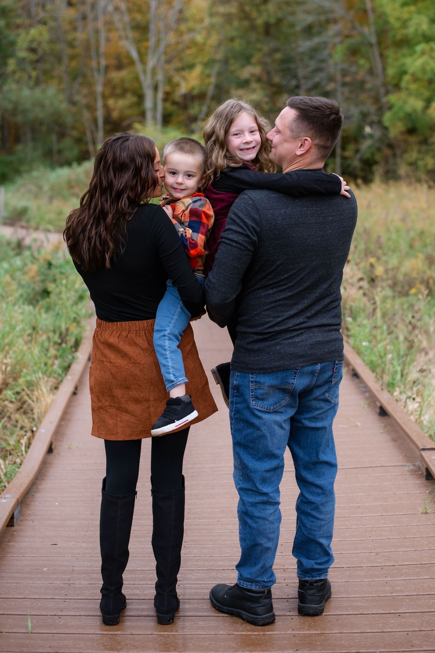 Family sharing intimate moment on wooden boardwalk surrounded by autumn scenery.