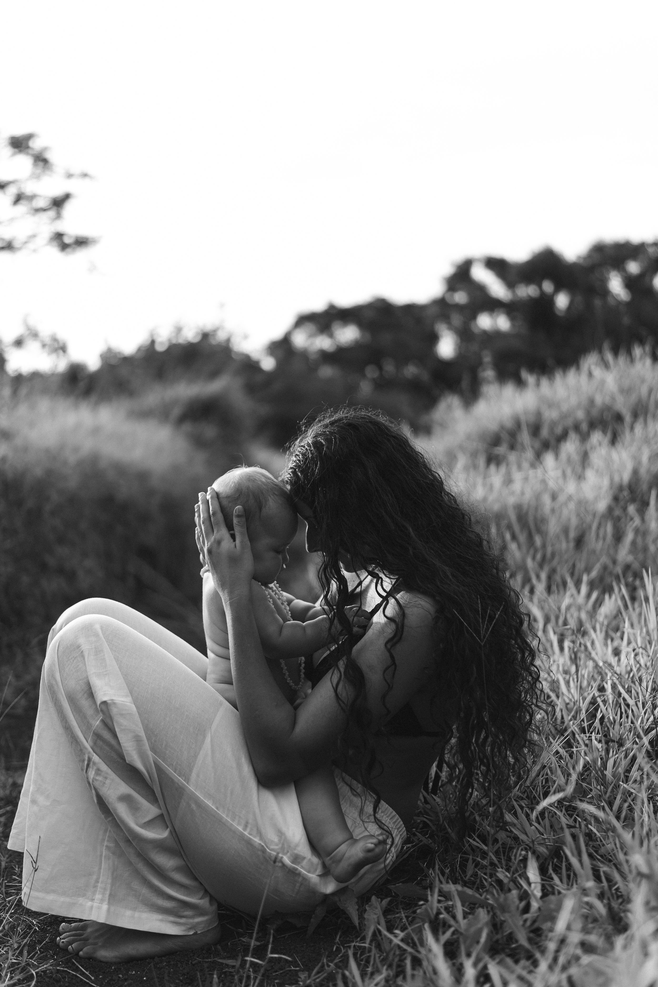 Woman sitting with her child in field with her head resting on her babies head – thoughtful black and white portrait