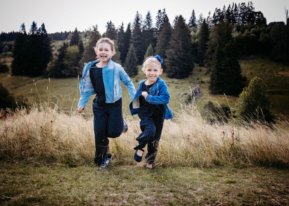 Children running playfully through a mountain meadow with evergreen forest backdrop.