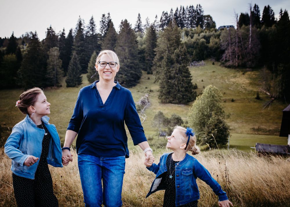 Family walks together through a scenic mountain meadow surrounded by evergreen forest.