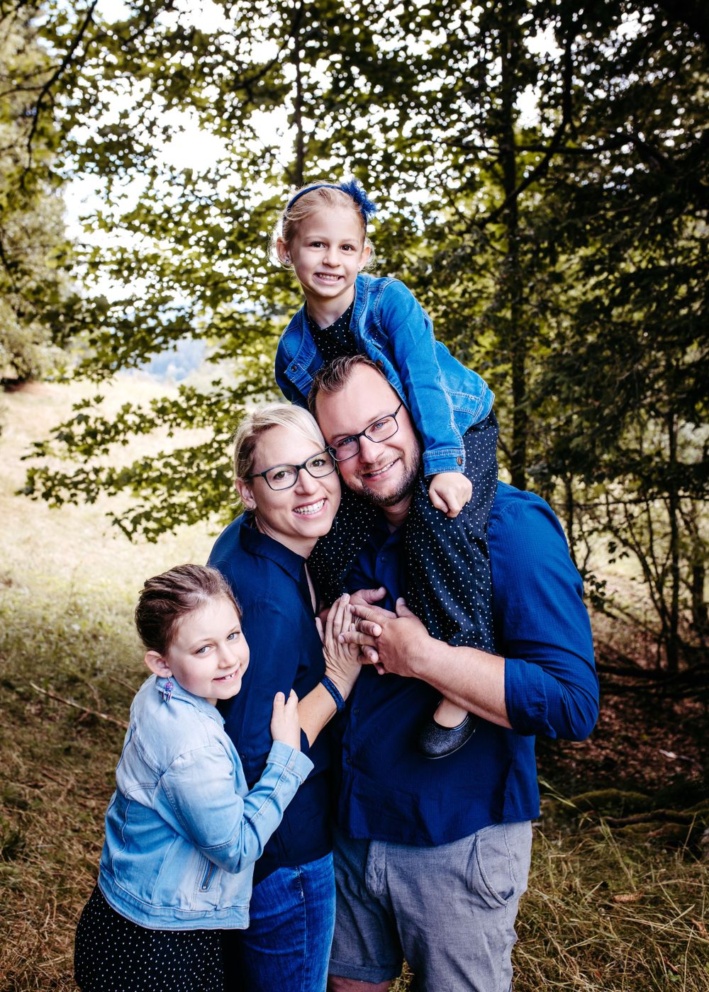 Family portrait with coordinating blue outfits in lush mountain setting.