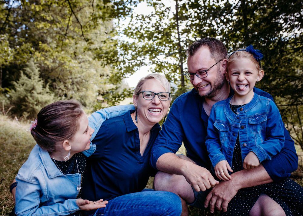 A joyful family wearing blue sits together outdoors sharing a laugh in a natural setting.