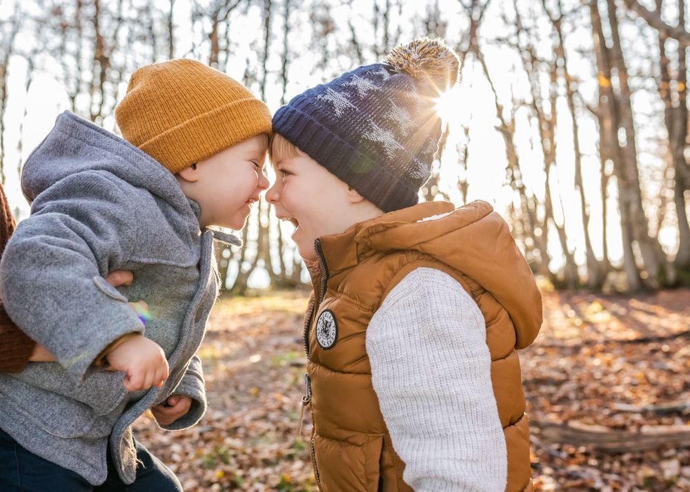 Sweet winter moment between two children wearing warm hats in the woods.