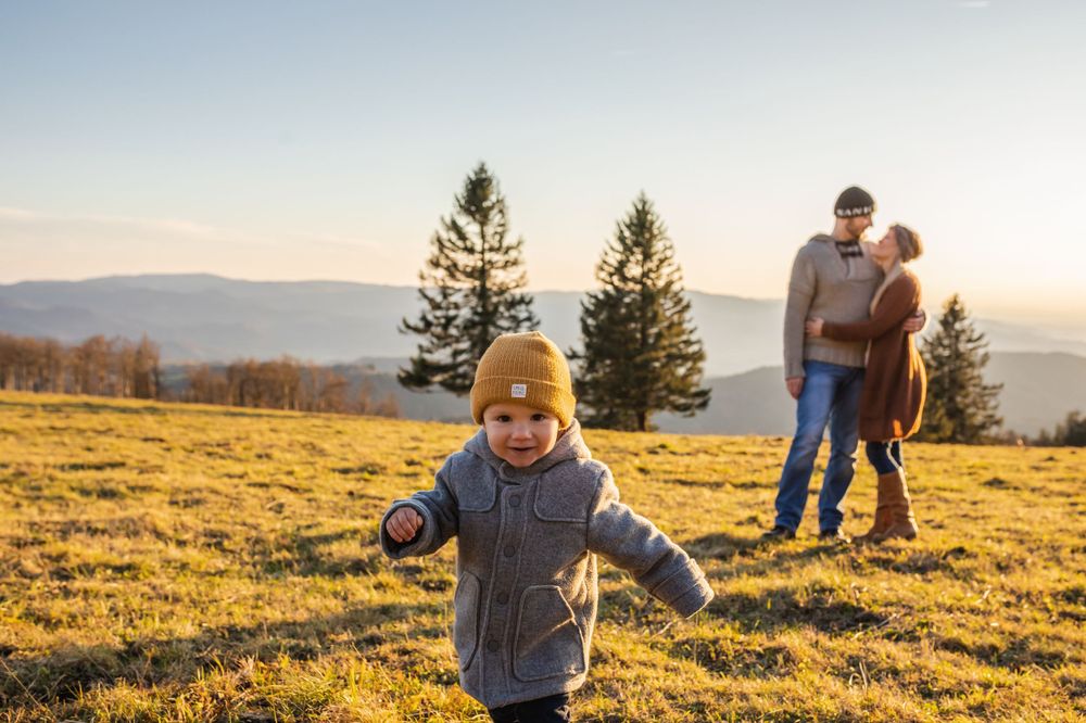 Child running joyfully through a sunlit mountain meadow while adults watch in the background.