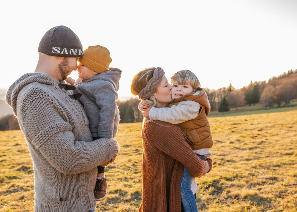 A loving family embraces during golden hour in an autumn field with mountains in the background.