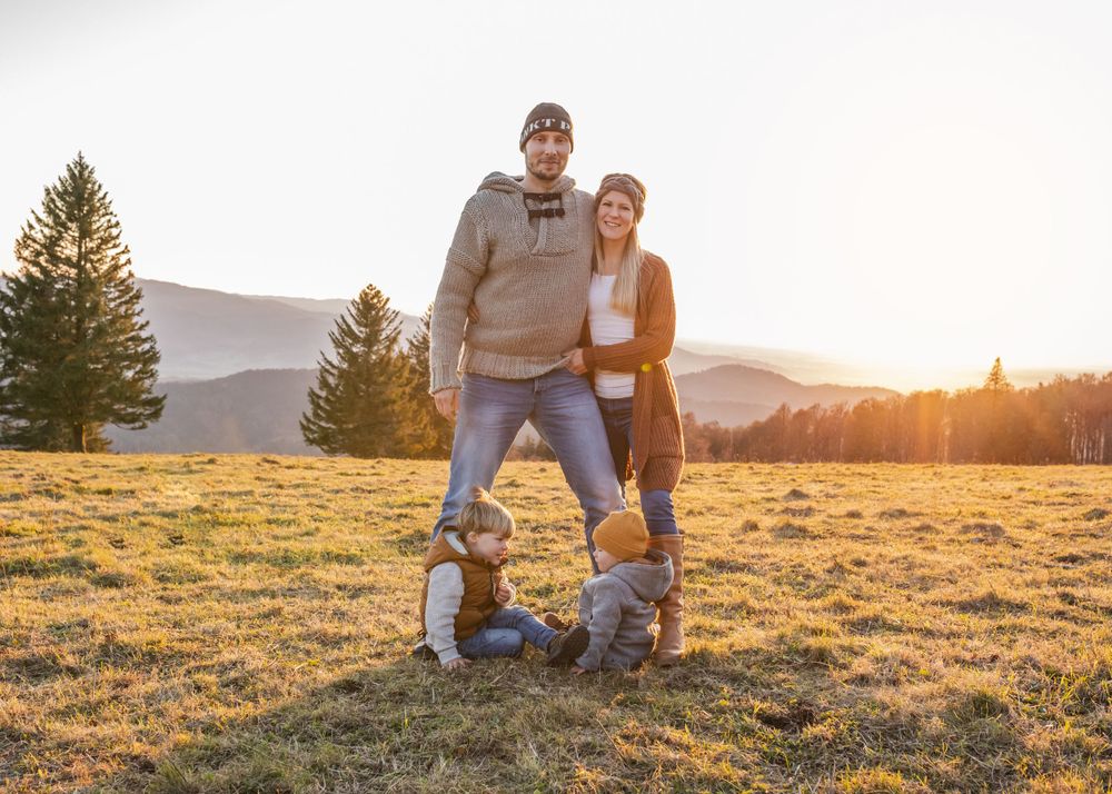 A family poses together at sunset in a mountainside meadow.