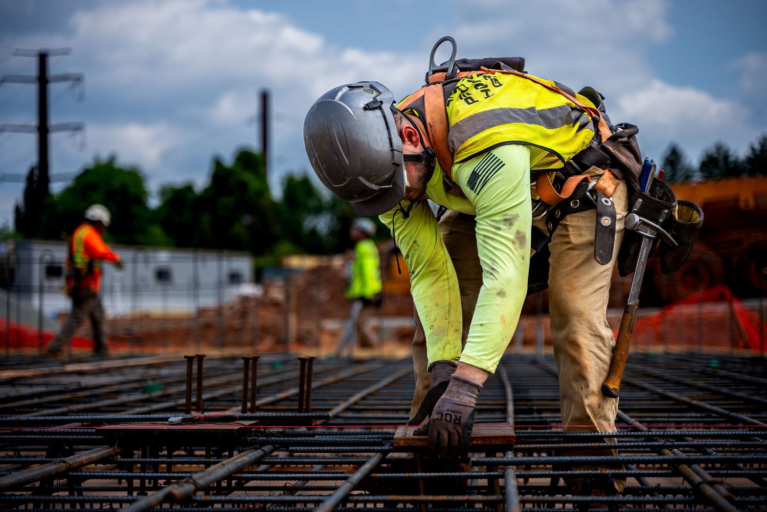 Construction worker in safety gear inspecting rebar grid framework at building site.