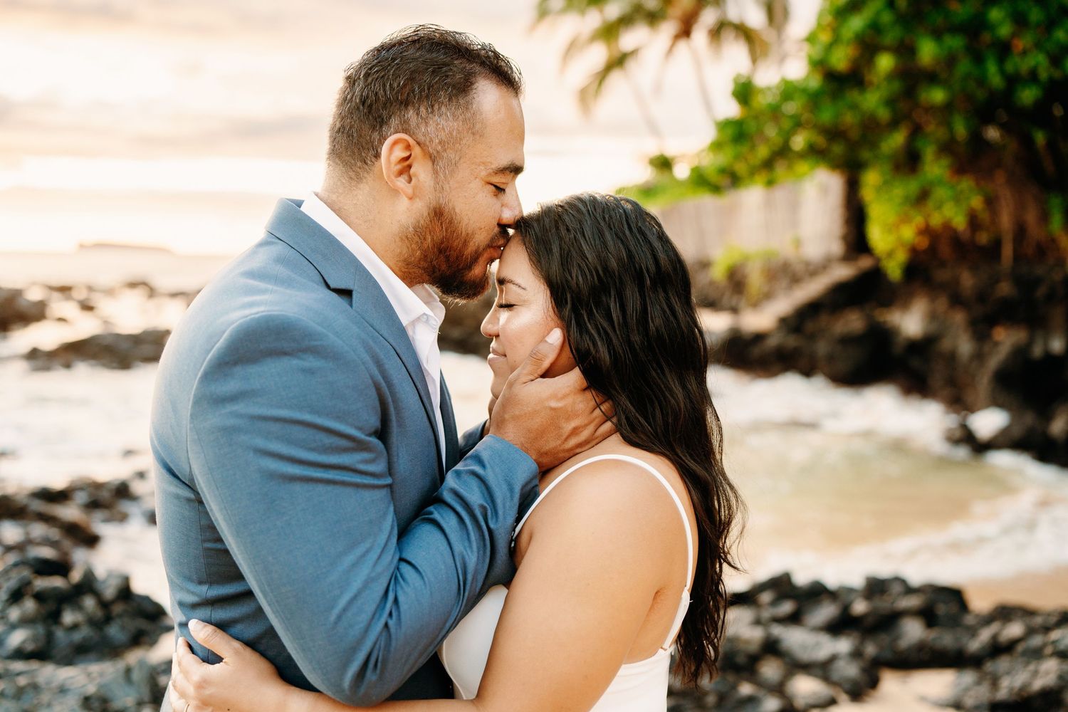 A romantic beach photoshoot with palm trees and ocean waves in the background.