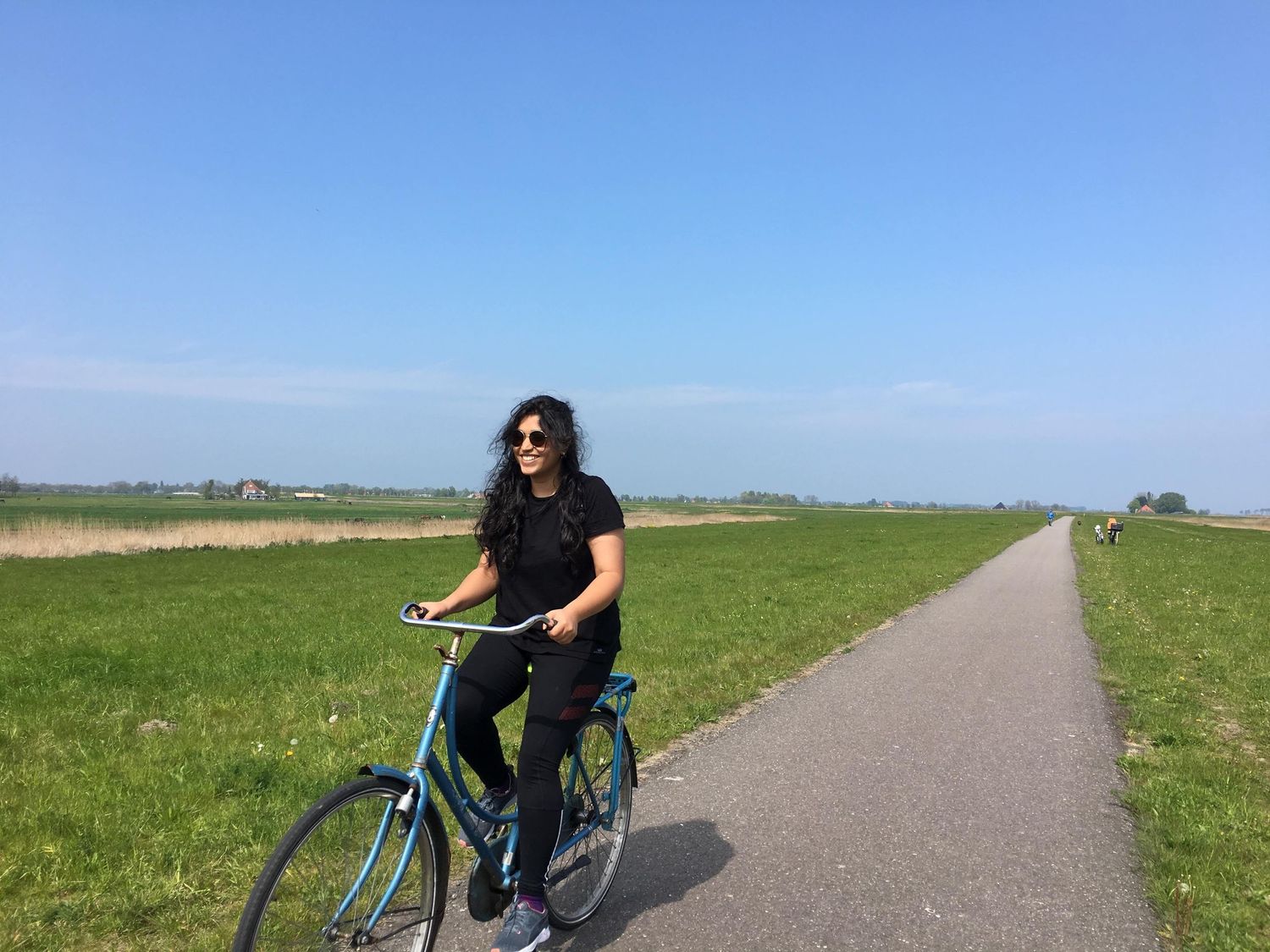 Nupur Nanal riding turquoise bicycle on rural path through green countryside.