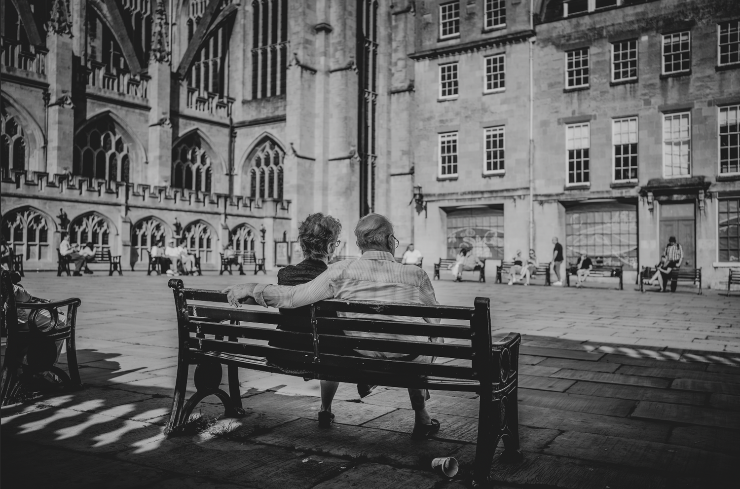 Person sitting alone on a bench outside a historic cathedral in black and white.