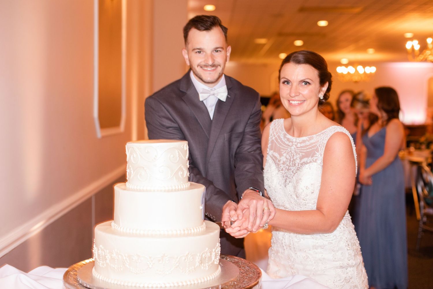 Wedding reception venue with tiered white cake and soft orange ambient lighting.