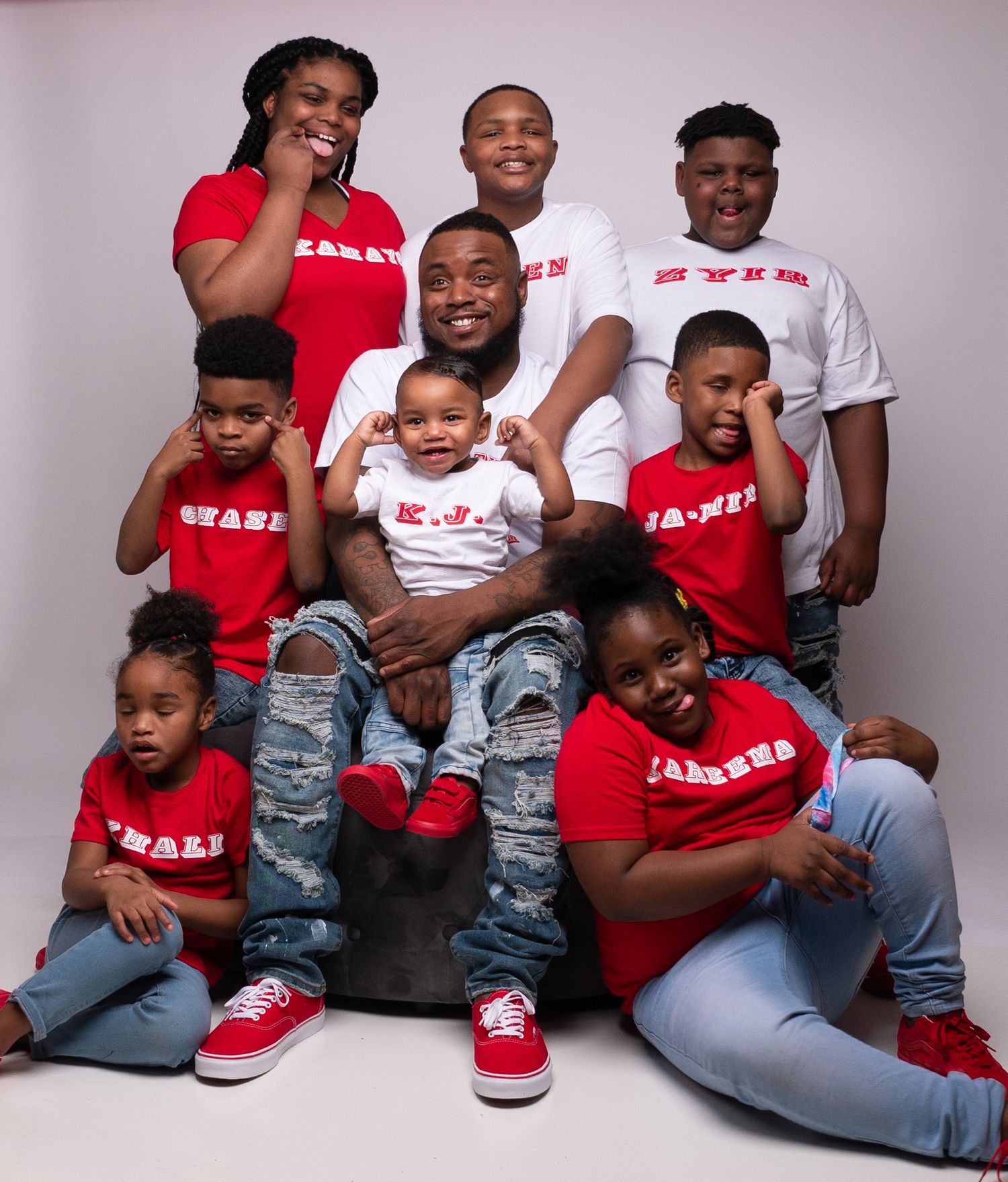 Studio portrait of family with matching red shirts and distressed jeans against light pink backdrop.
