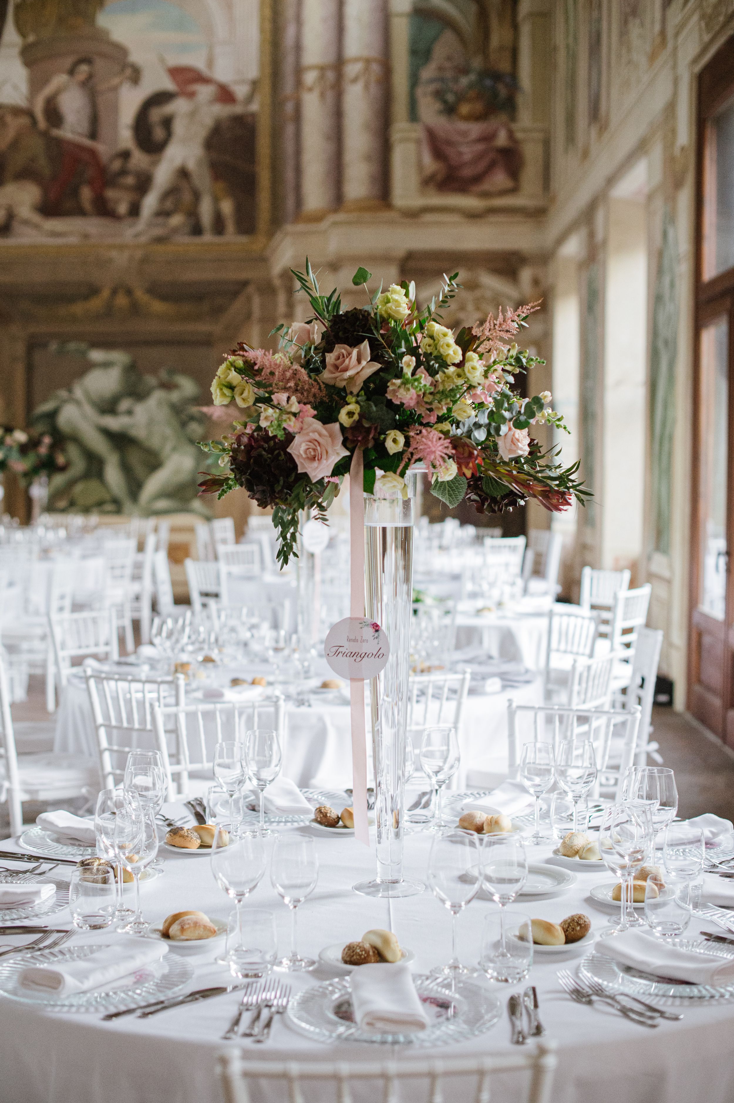 Elegant wedding table setting with tall floral centerpiece in ornate historic venue.