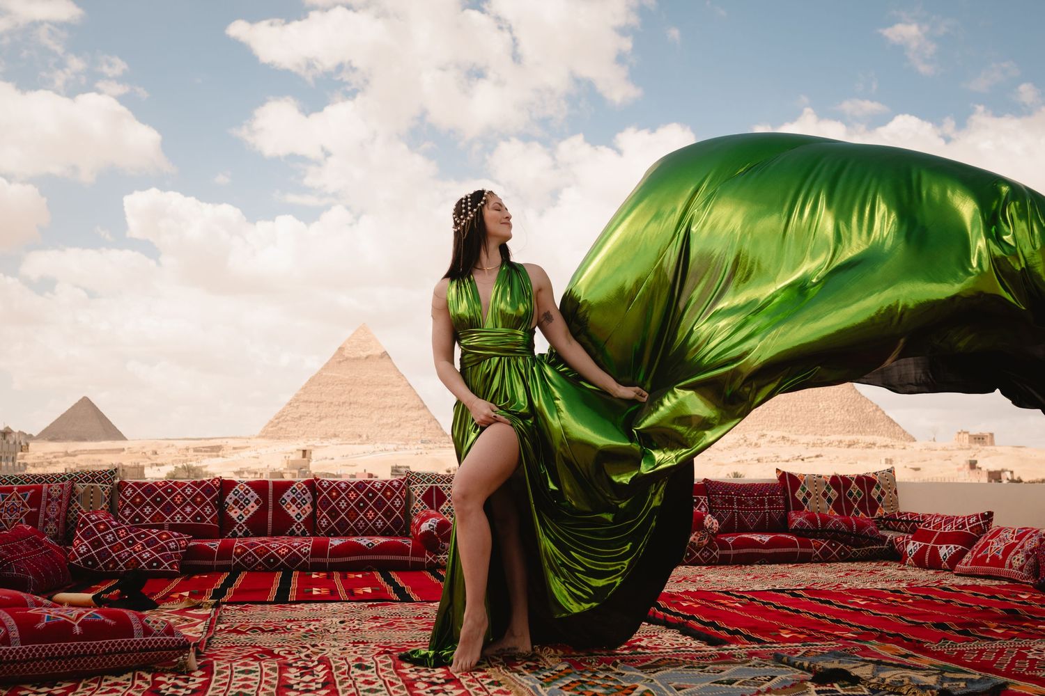 Billowing green dress catches wind on rooftop with ancient pyramids in distance.