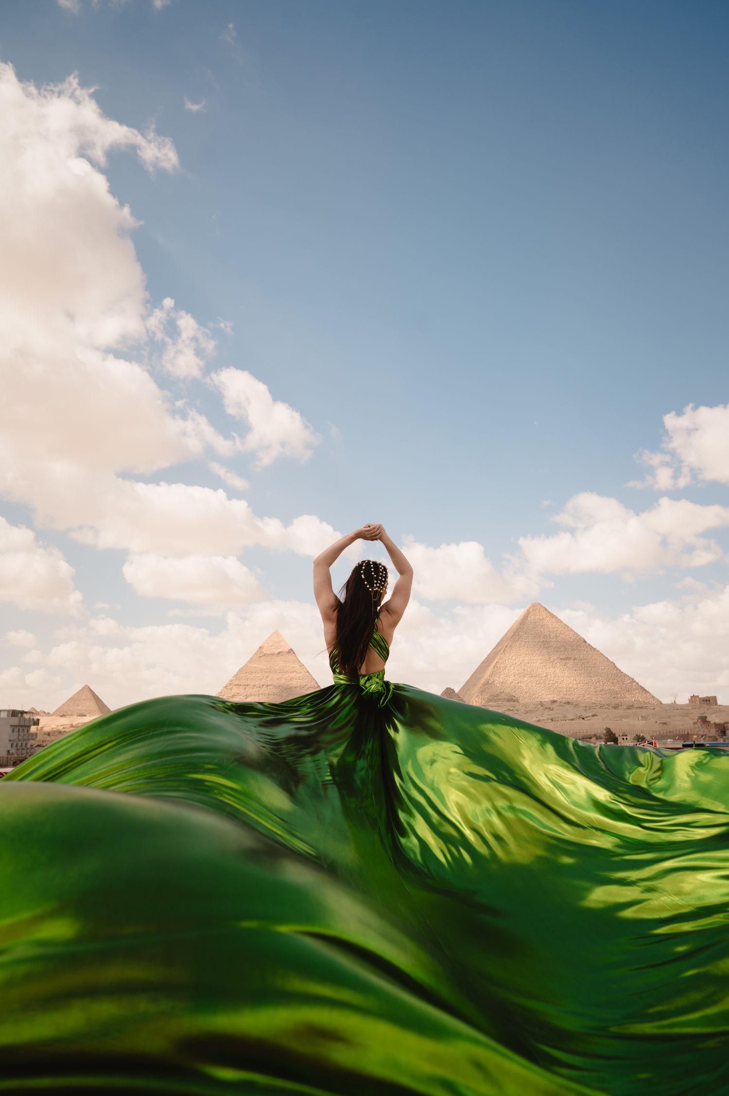 Dramatic flowing green fabric creates waves against Egyptian pyramid backdrop.