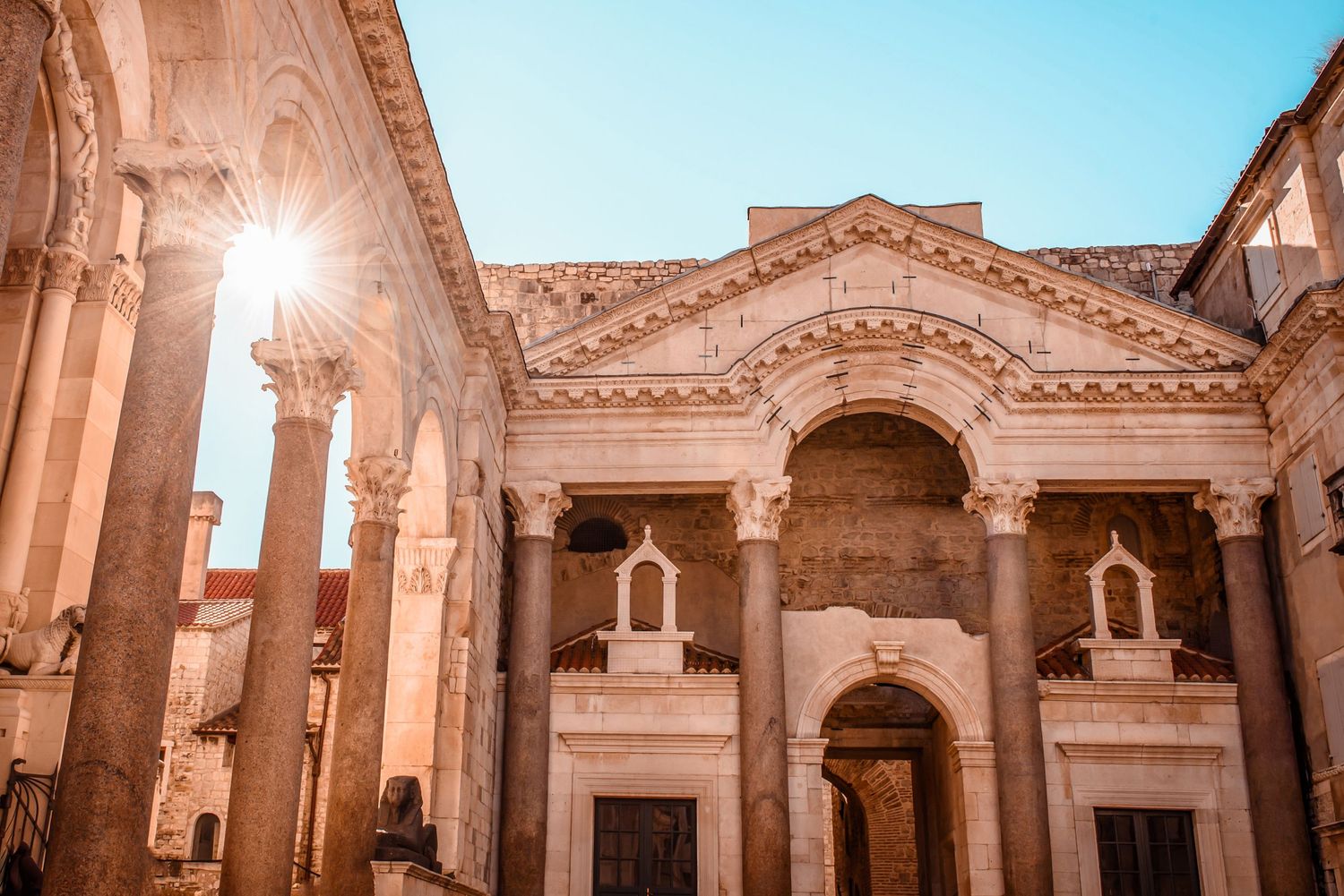 Sunlit ancient Roman architecture featuring ornate columns and arched entrances.