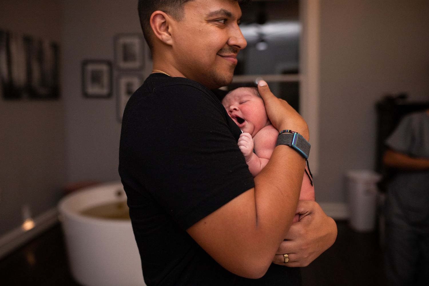 Happy Dad is smiling and holding brand new baby at Origins Birth and Wellness Dallas Texas