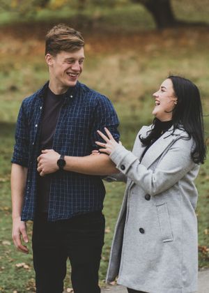 A couple sharing a heartfelt laugh together during an autumn photoshoot in a park setting.