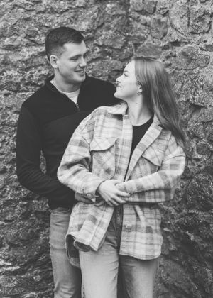 A loving couple shares a joyful moment against a stone wall background in black and white photography.