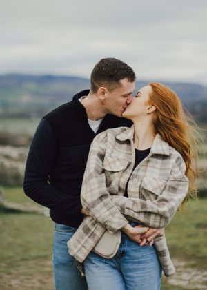 A romantic moment captured between a couple kissing on a hilltop with rolling landscapes in the background.