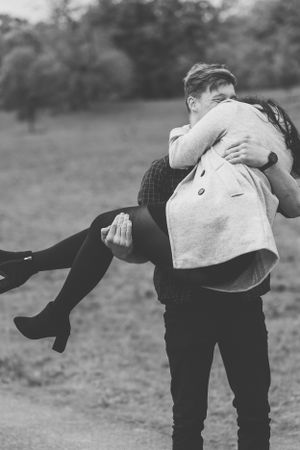 A playful black and white photo of a couple during a romantic lift pose in a field.