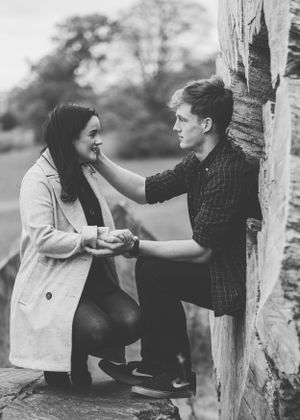 A tender black and white moment between a couple by a rustic wooden wall during what appears to be a proposal.