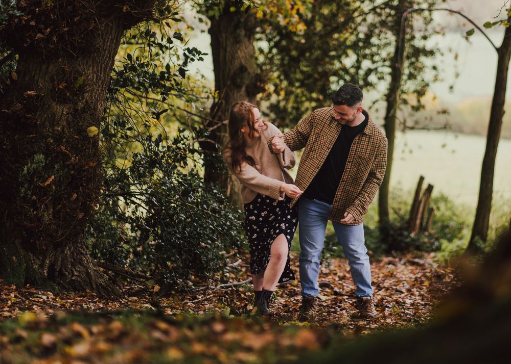 Couple sharing intimate autumn moment among fallen leaves by lakeside.