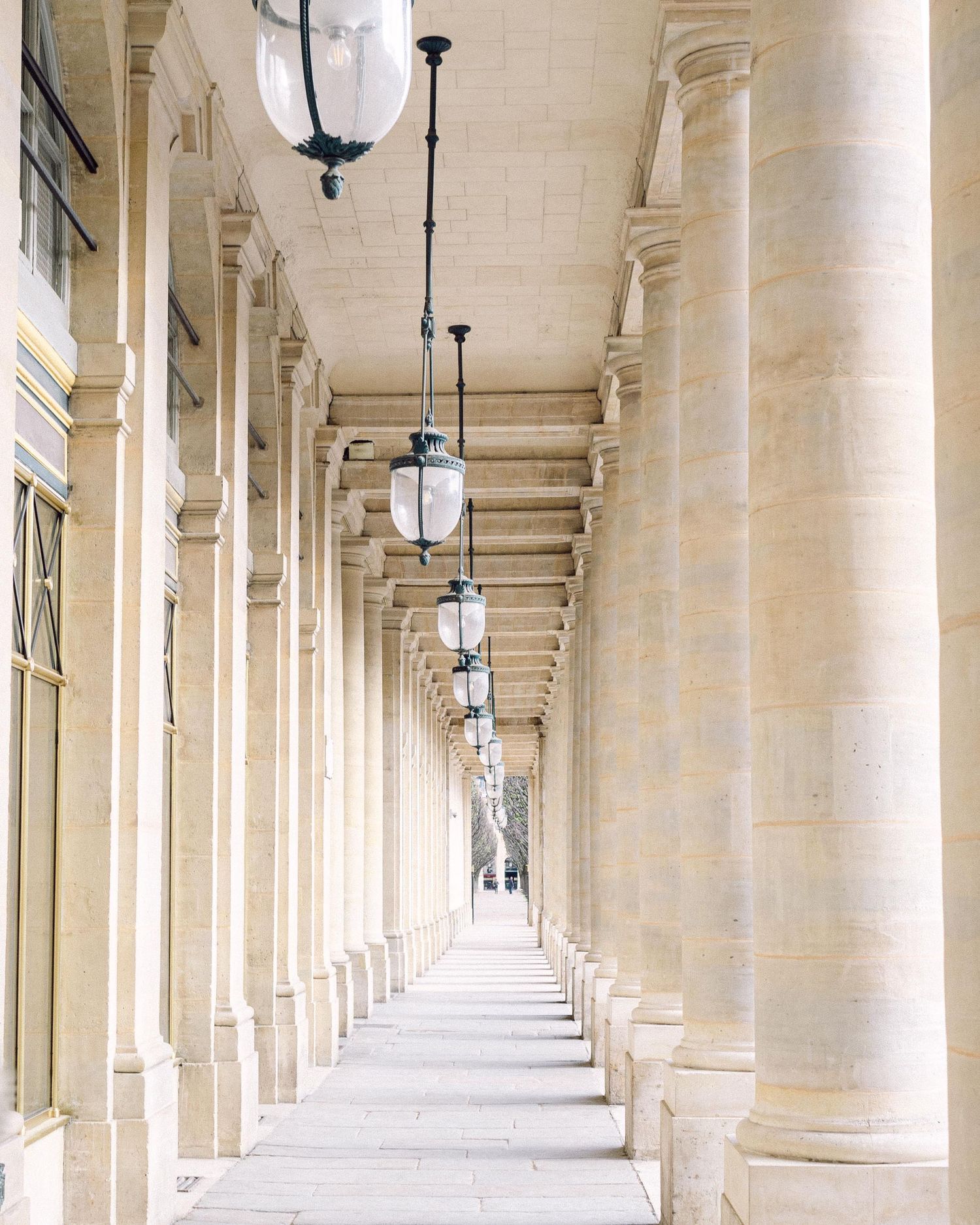 White stone colonnade hallway with hanging lanterns creating a dramatic vanishing point perspective in classical architecture.