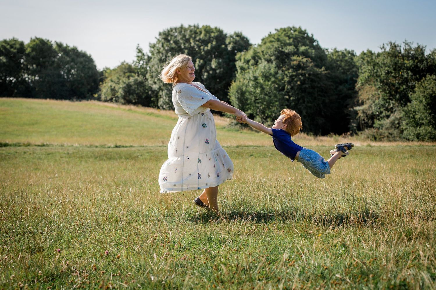 mother swinging boy child round in the air on a summer day.. They are both laughing