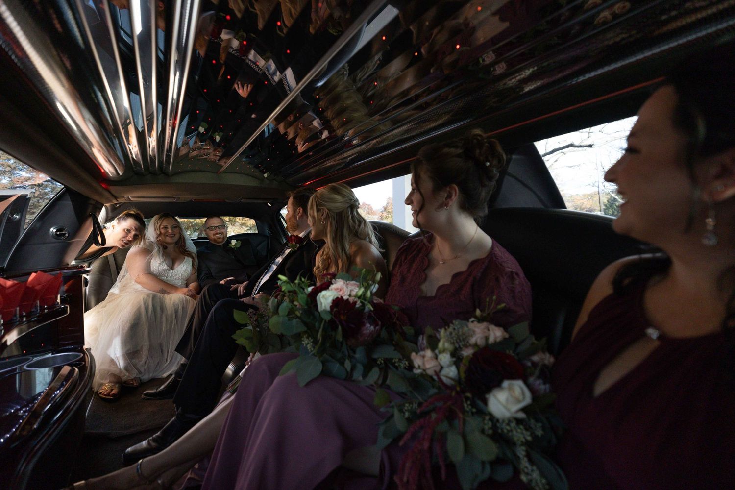Wedding party riding in limousine with floral bouquets visible in dramatic lighting.