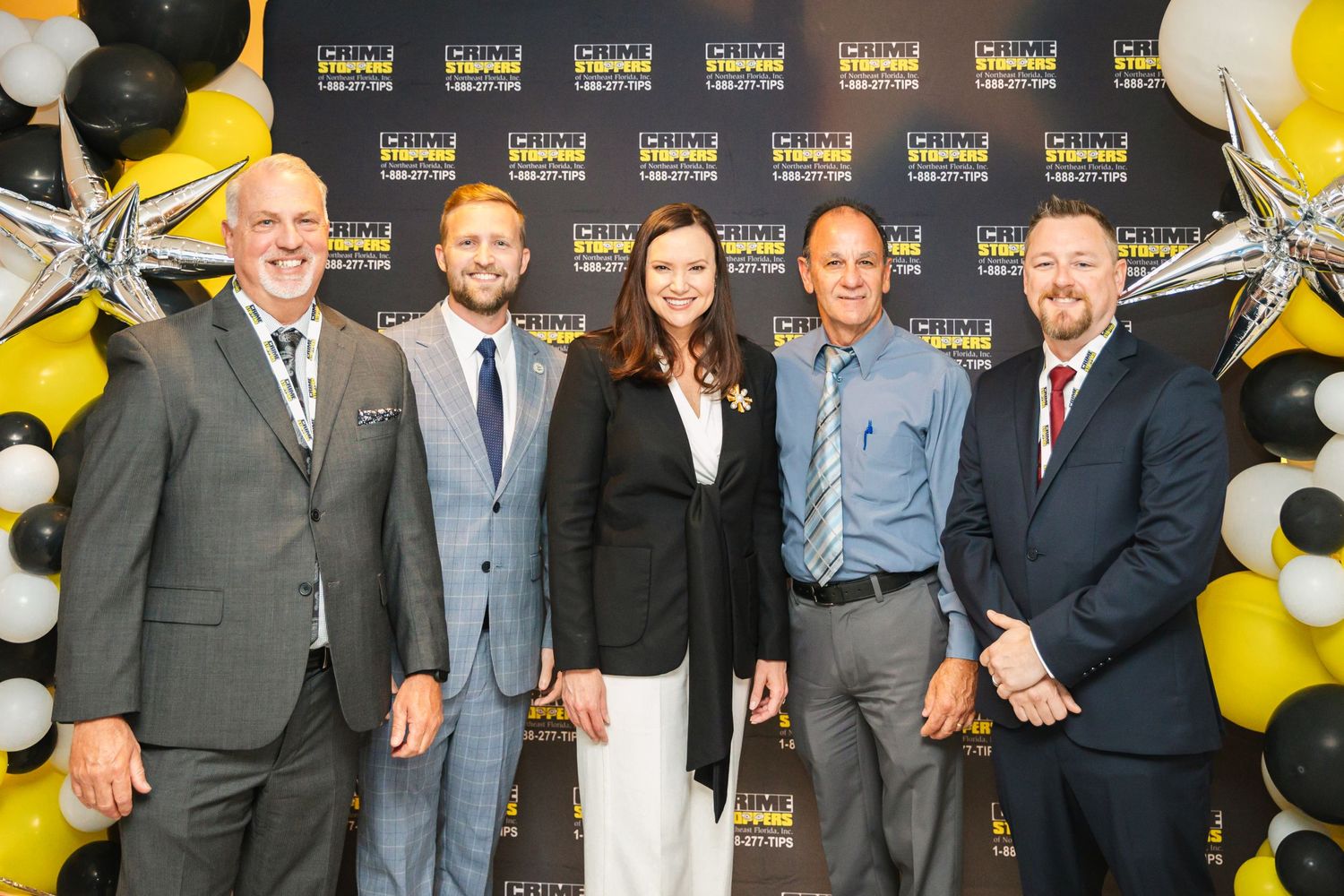 Professional group poses at corporate event with black and gold balloon decorations.