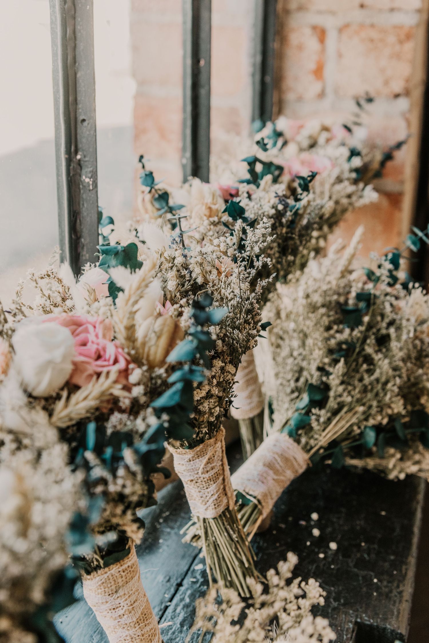 Rustic dried flower bouquet wrapped in burlap and twine against an industrial window frame.