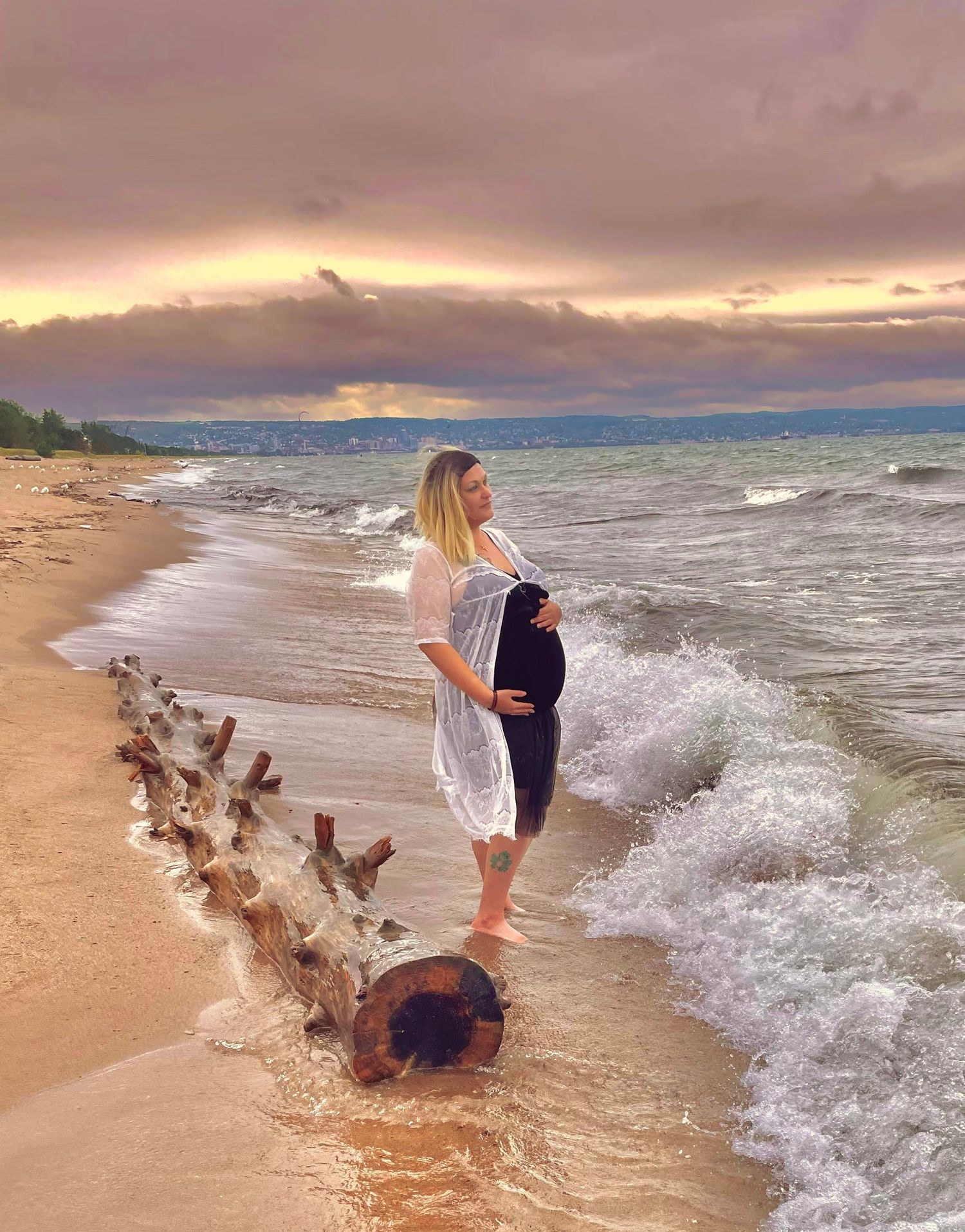 Scenic beach maternity photo at sunset with waves crashing on shore.