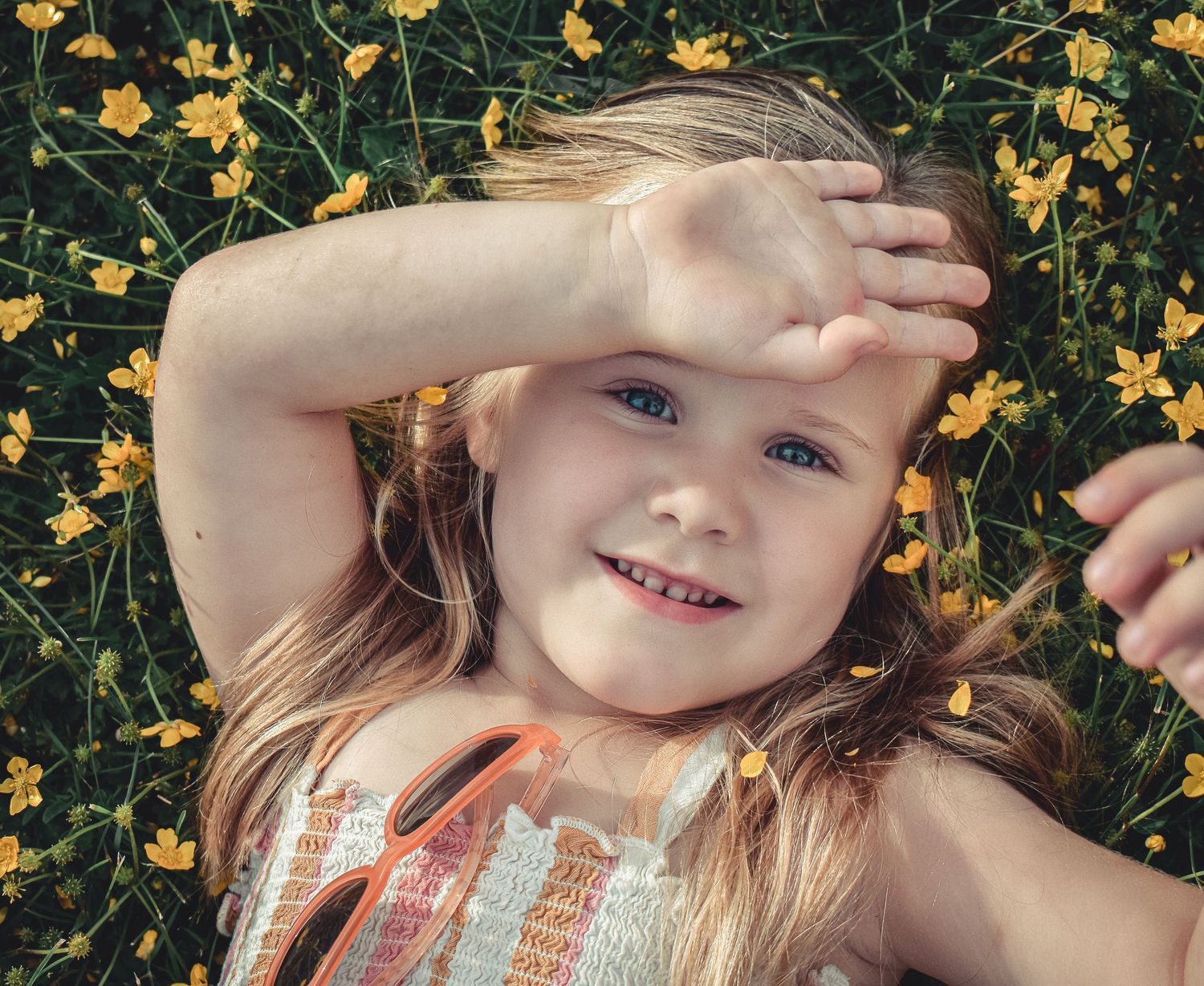 Child lying in field of yellow wildflowers shielding eyes from sun.